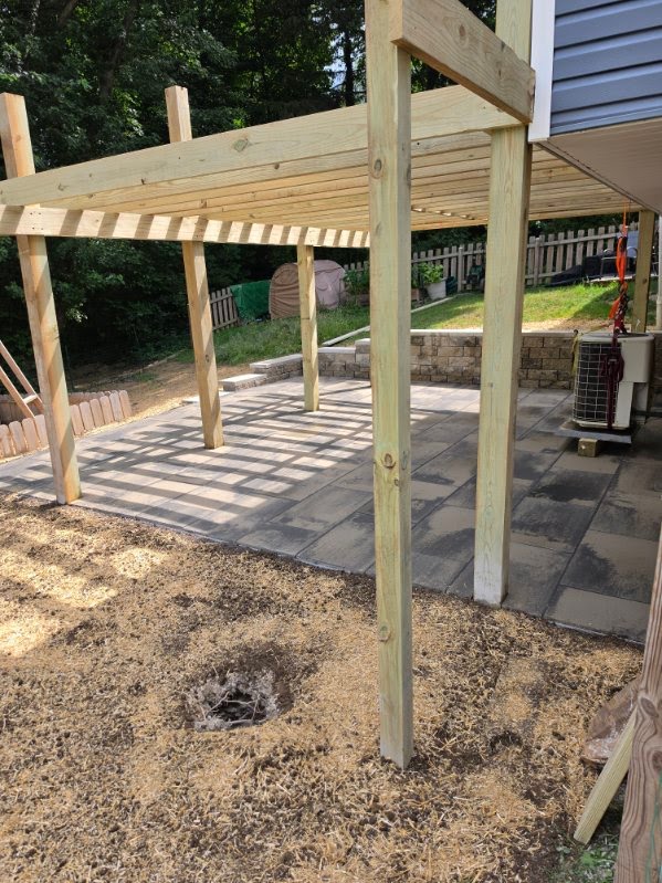 Cedar pergola frame over a new paver patio with stone wall behind